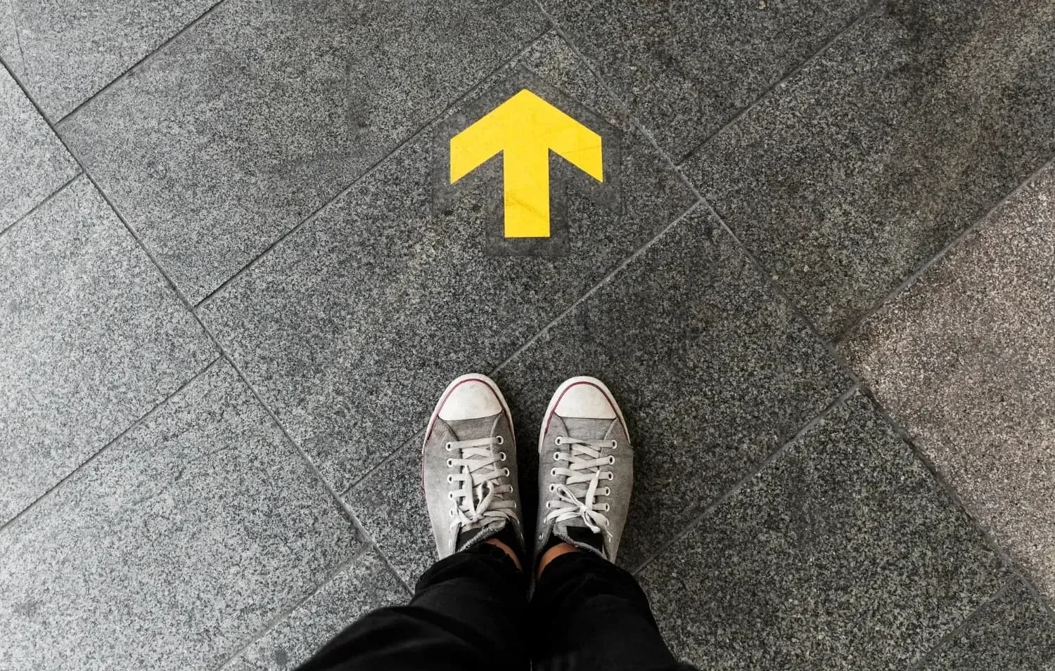 Student standing at a yellow arrow painted on a paved walkway, pointing forward