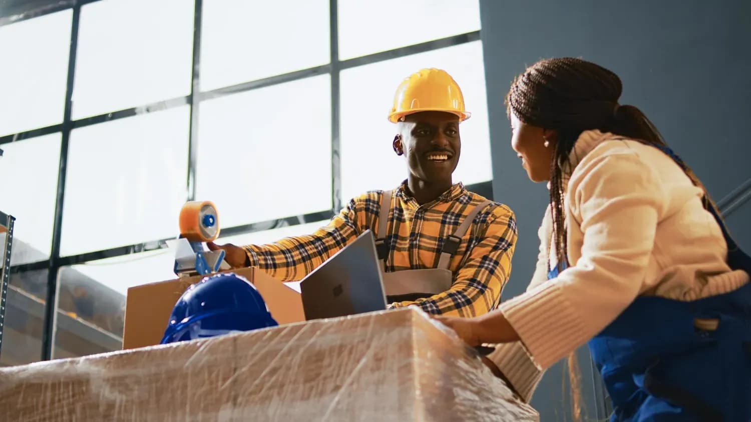 Two young artisans in workwear and a hard hat checking stock in a warehouse
