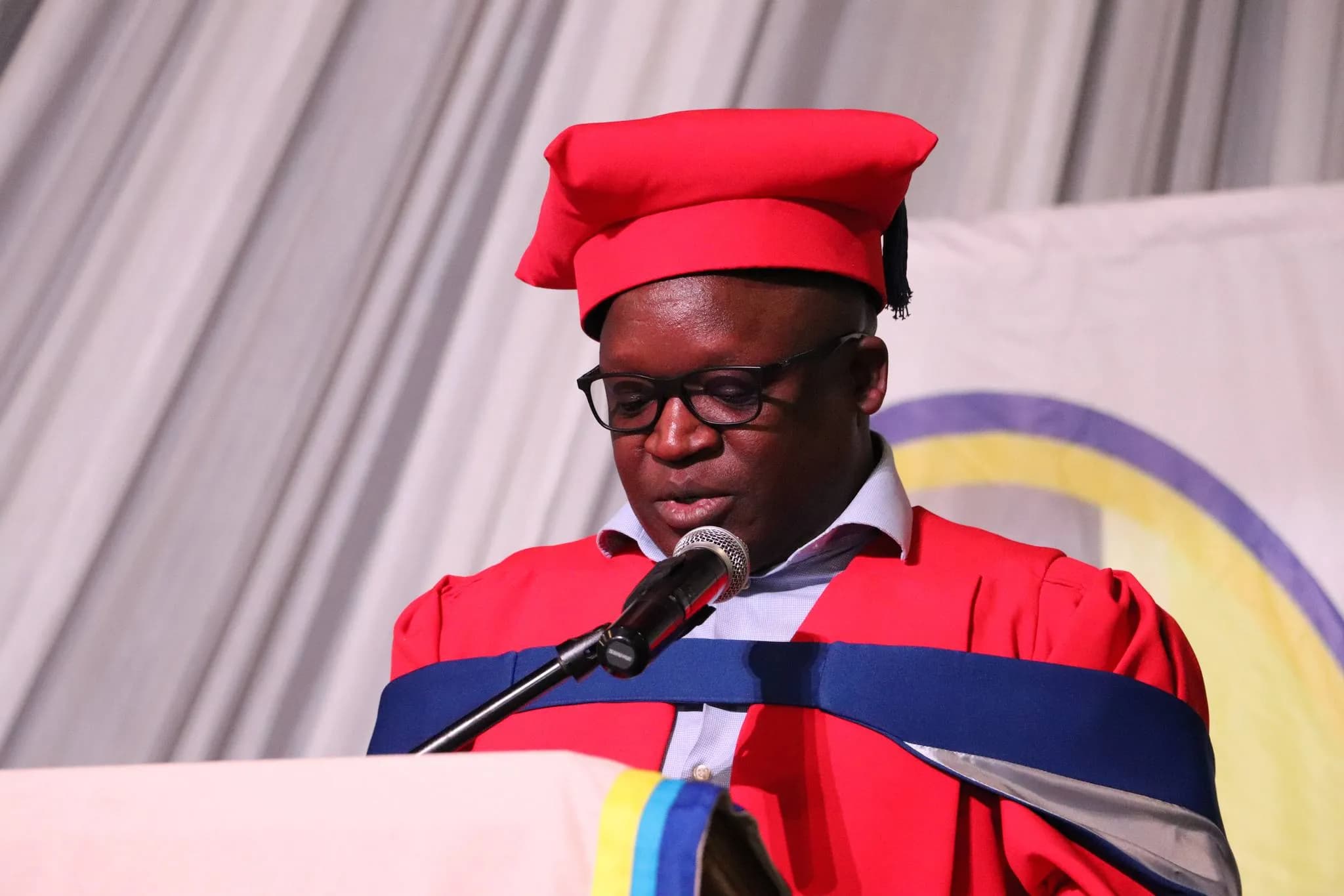 Speaker in red graduation regalia addressing a ceremony