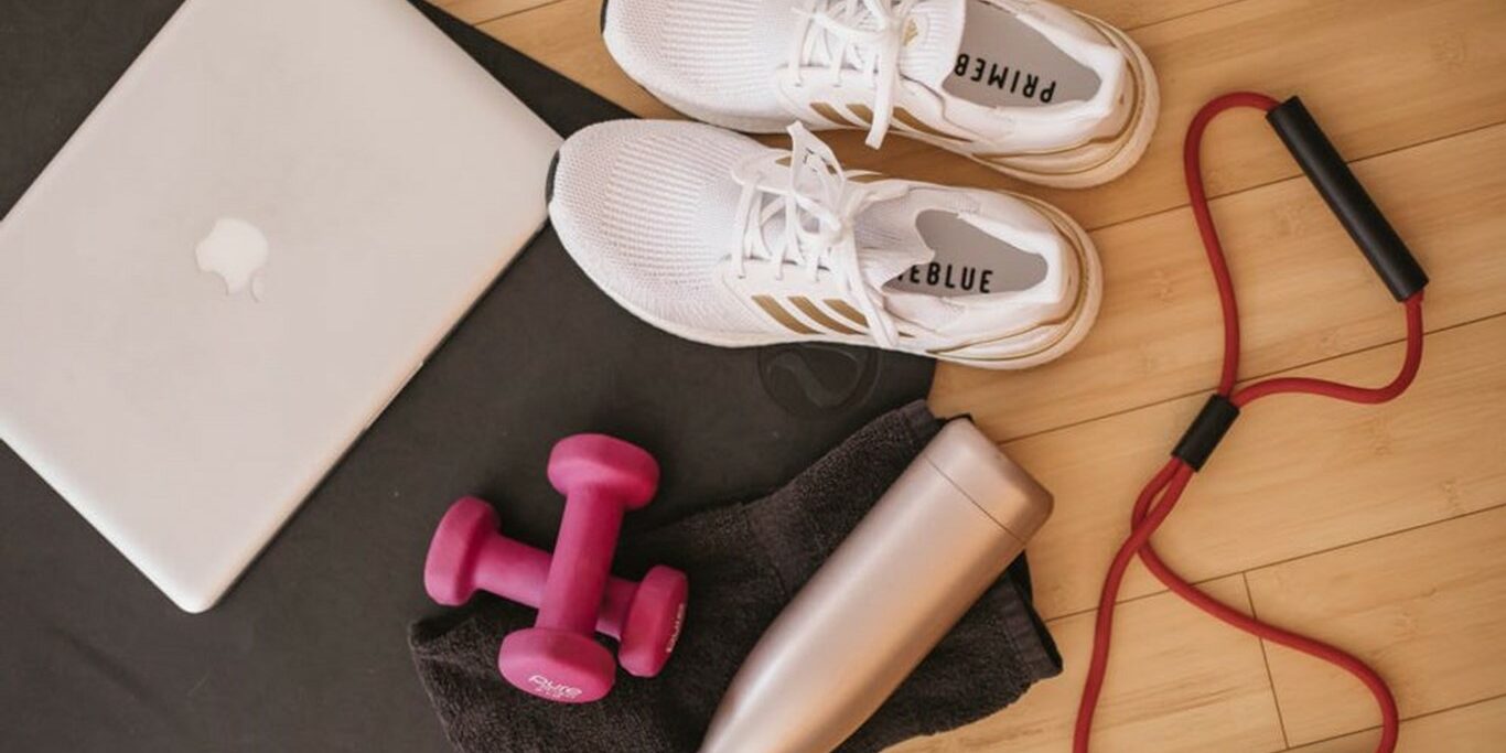 An image a water bottle, pink dumbbells, a laptop and earphones